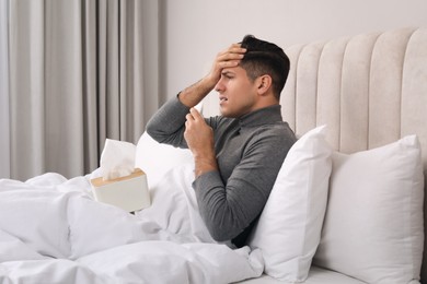 Sick man with box of paper tissues suffering from cold in bed at home