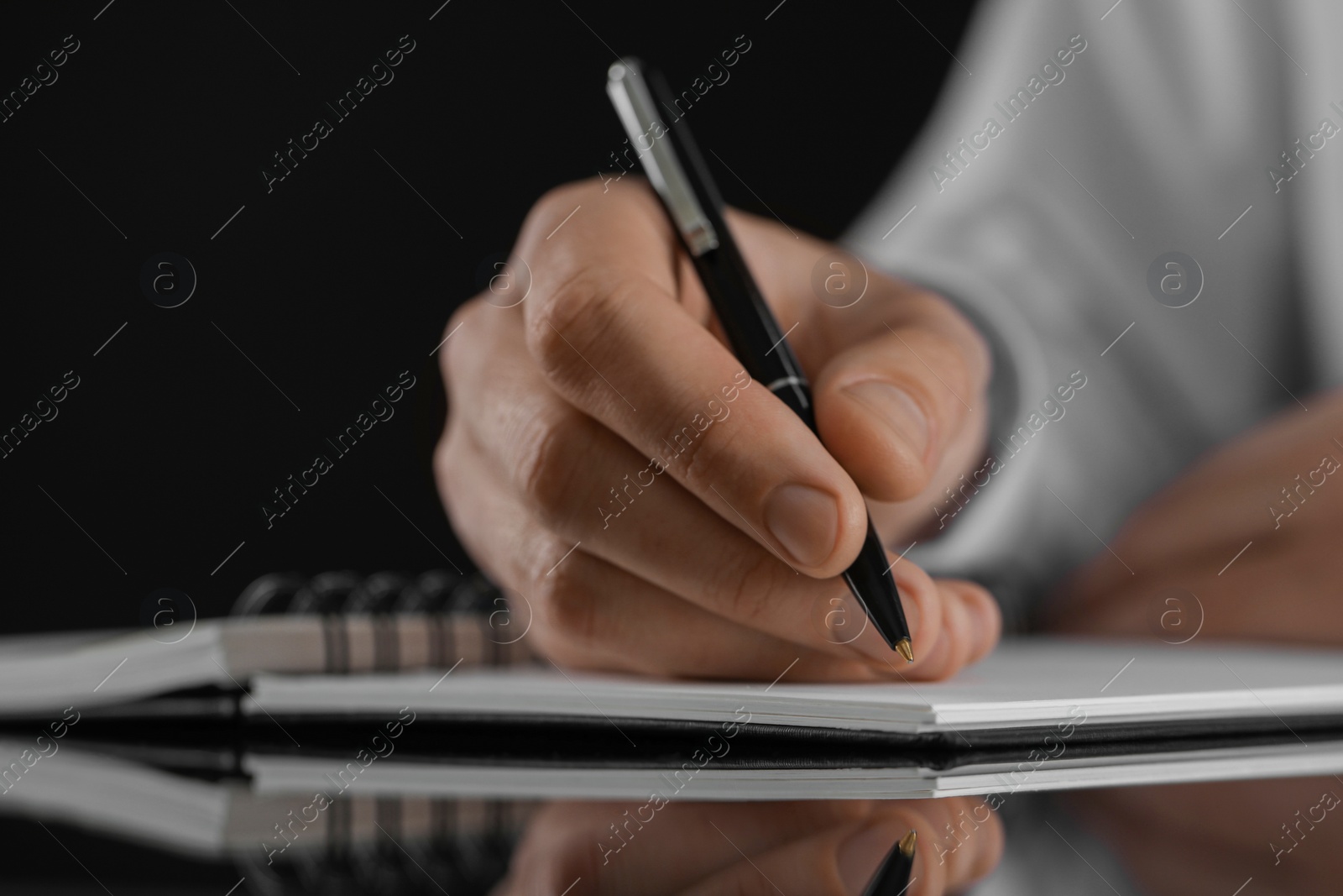 Photo of Man writing in notebook at black table, closeup