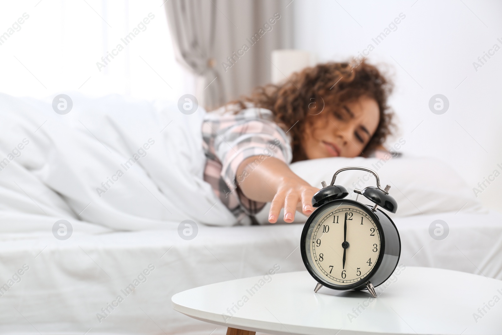 Photo of Young African-American woman turning off alarm clock at home. Bedtime