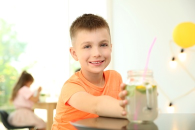 Photo of Little boy with natural lemonade at table indoors