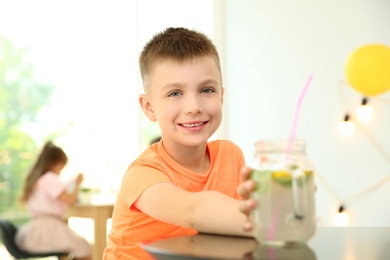 Little boy with natural lemonade at table indoors