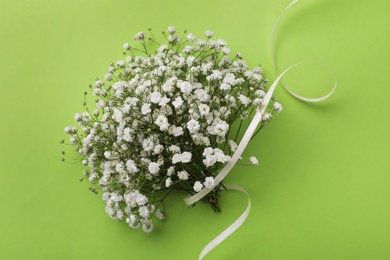 Beautiful bouquet of white gypsophila flowers with ribbon on light green background, top view