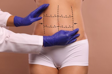 Image of Doctor and patient preparing for cosmetic surgery, light brown background. Woman with markings on her abdomen, closeup