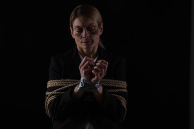 Photo of Woman tied up and taken hostage on dark background. Space for text