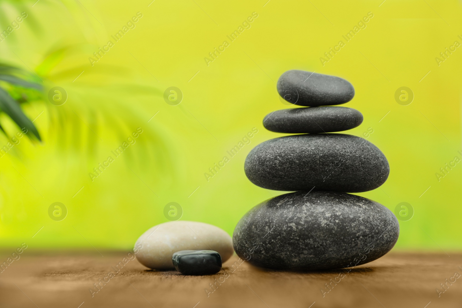 Photo of Table with stack of stones and blurred green leaves on background, space for text. Zen concept