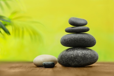 Table with stack of stones and blurred green leaves on background, space for text. Zen concept