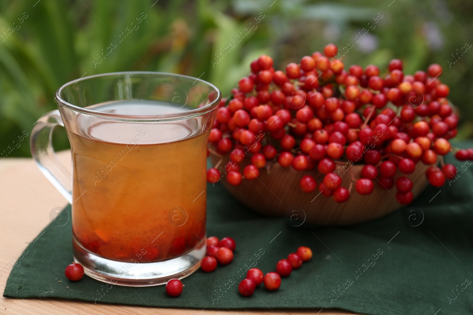 Photo of Cup of tea and fresh ripe viburnum berries on table outdoors