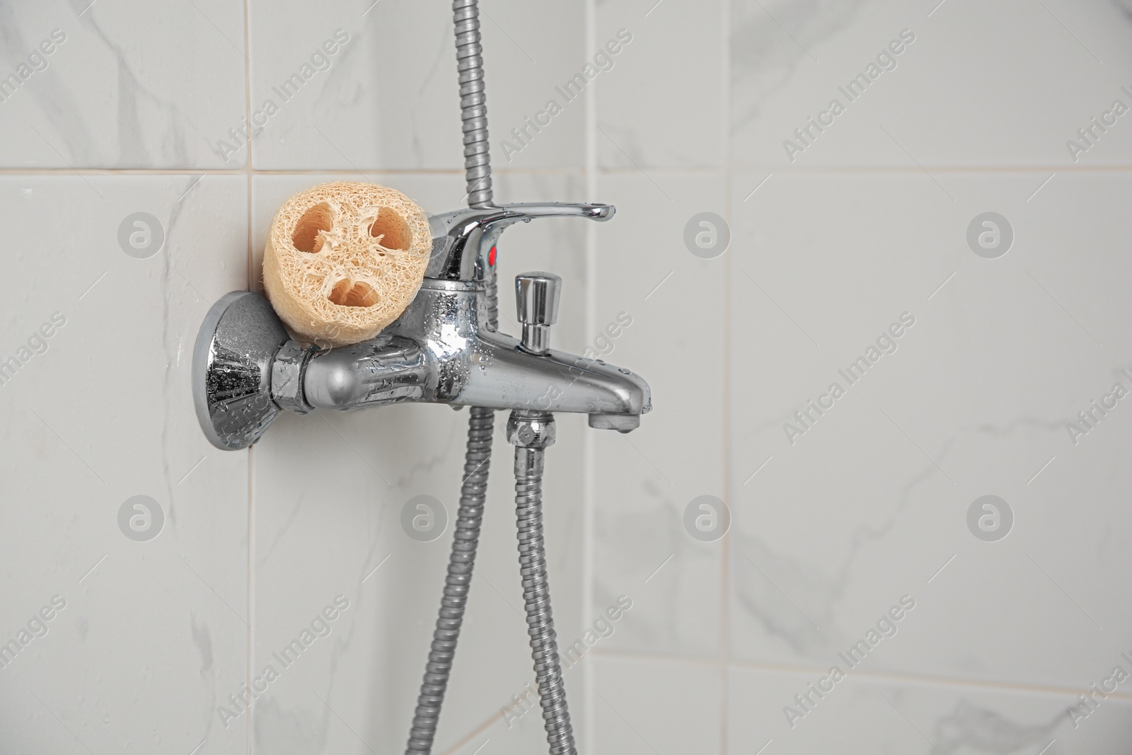 Photo of Natural loofah sponge on faucet in bathroom, space for text