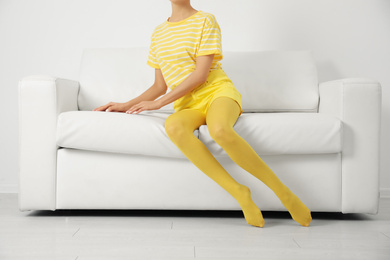 Woman wearing yellow tights sitting on sofa indoors, closeup