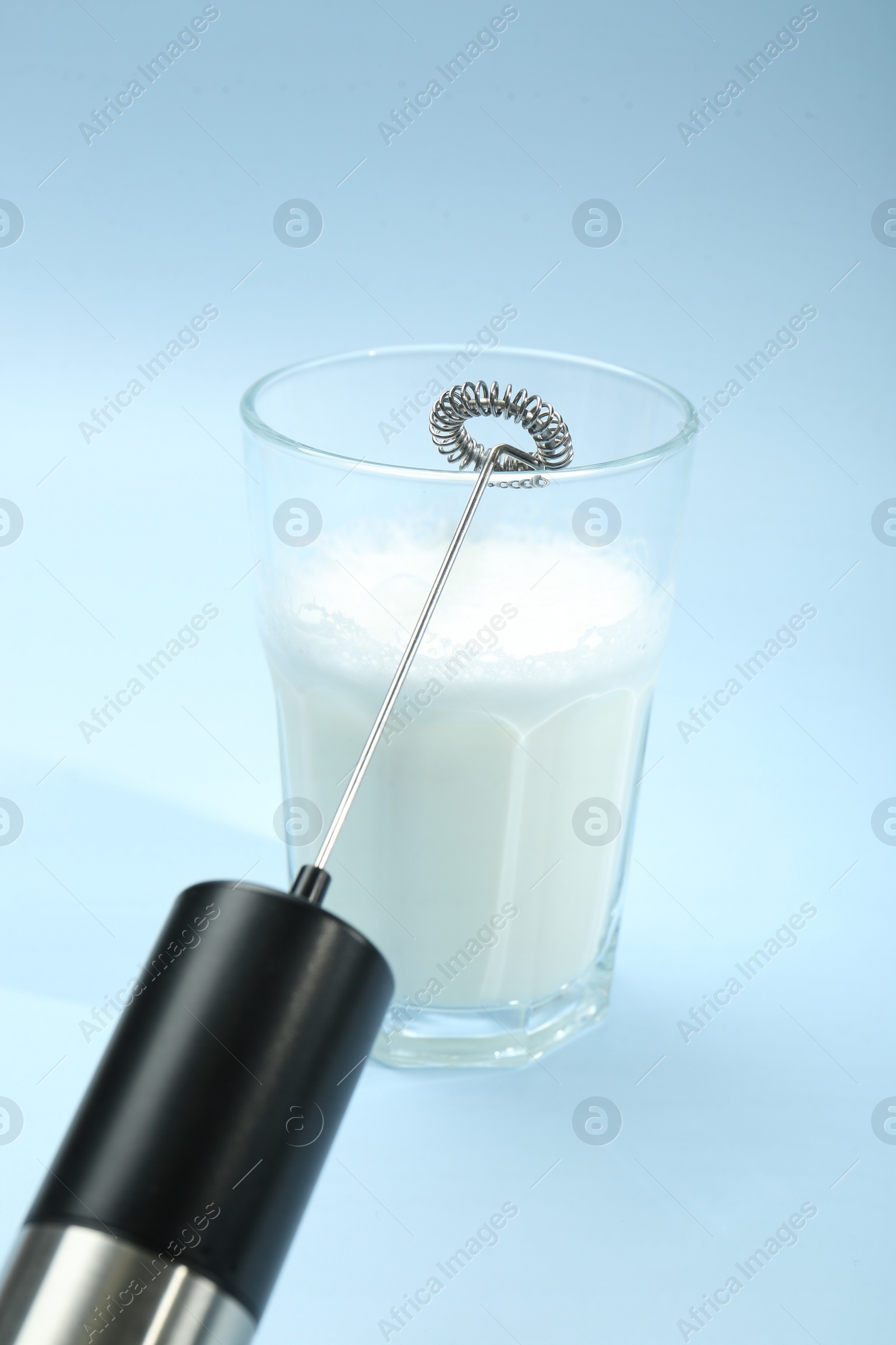 Photo of Mini mixer (milk frother) and whipped milk in glass on light blue background