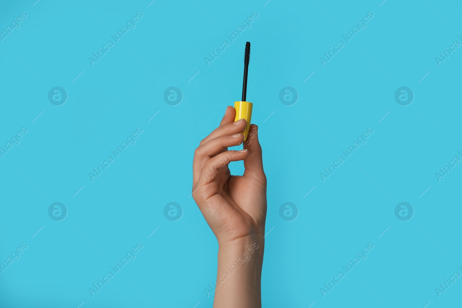 Photo of Woman holding mascara for eyelashes on light blue background, closeup