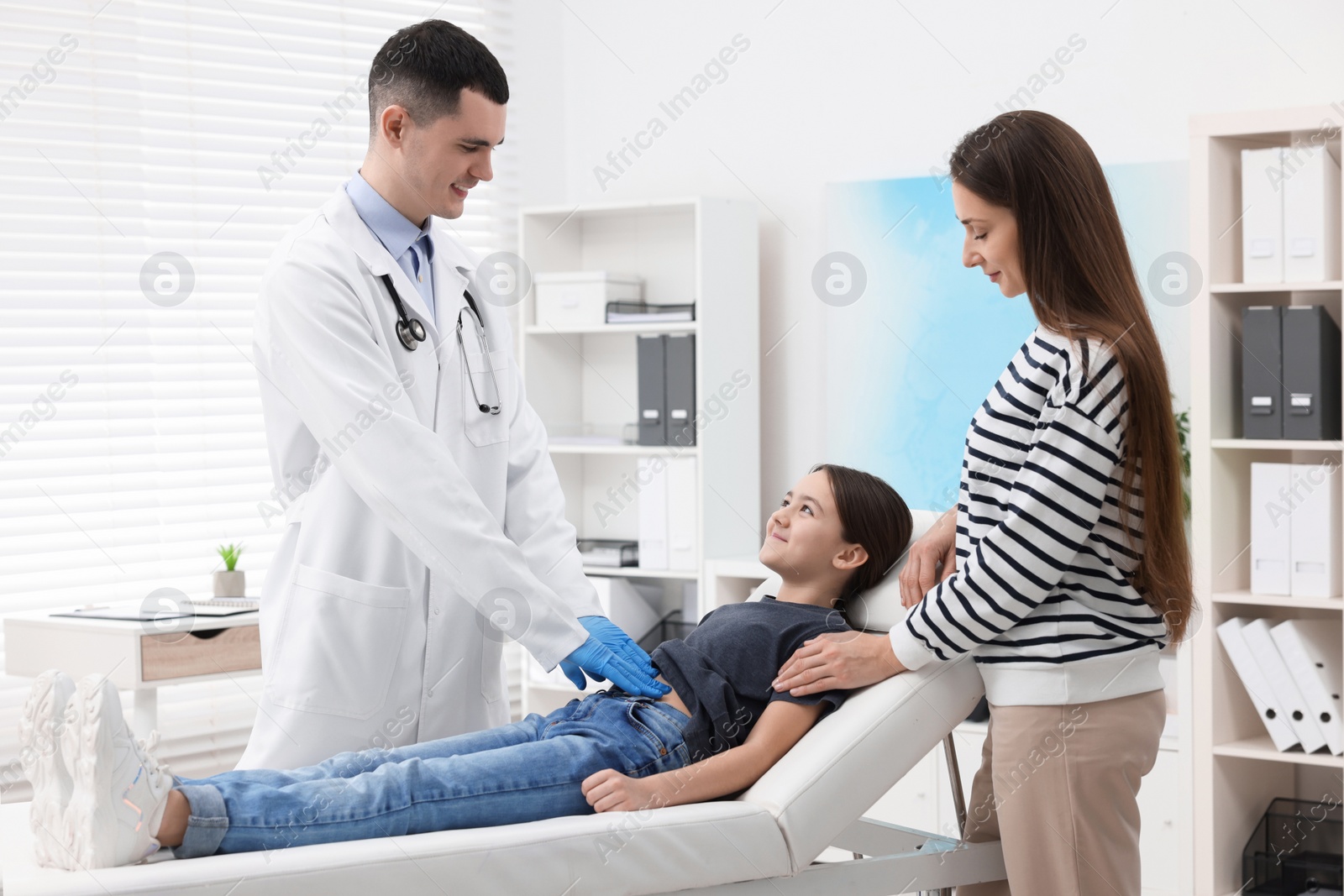 Photo of Gastroenterologist examining girl with stomach ache on couch in clinic