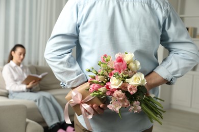 Man hiding bouquet of flowers and present for his beloved woman indoors, closeup