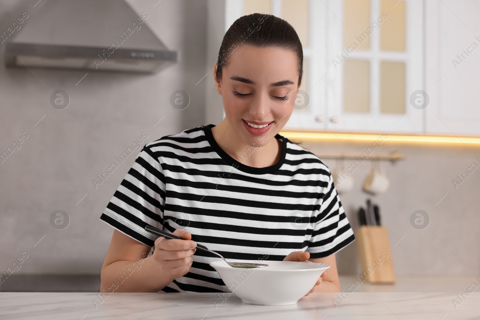 Photo of Woman eating tasty soup at white table in kitchen