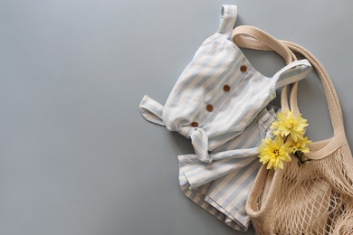 Photo of Stylish child clothes, flowers and mesh bag on grey background, flat lay. Space for text