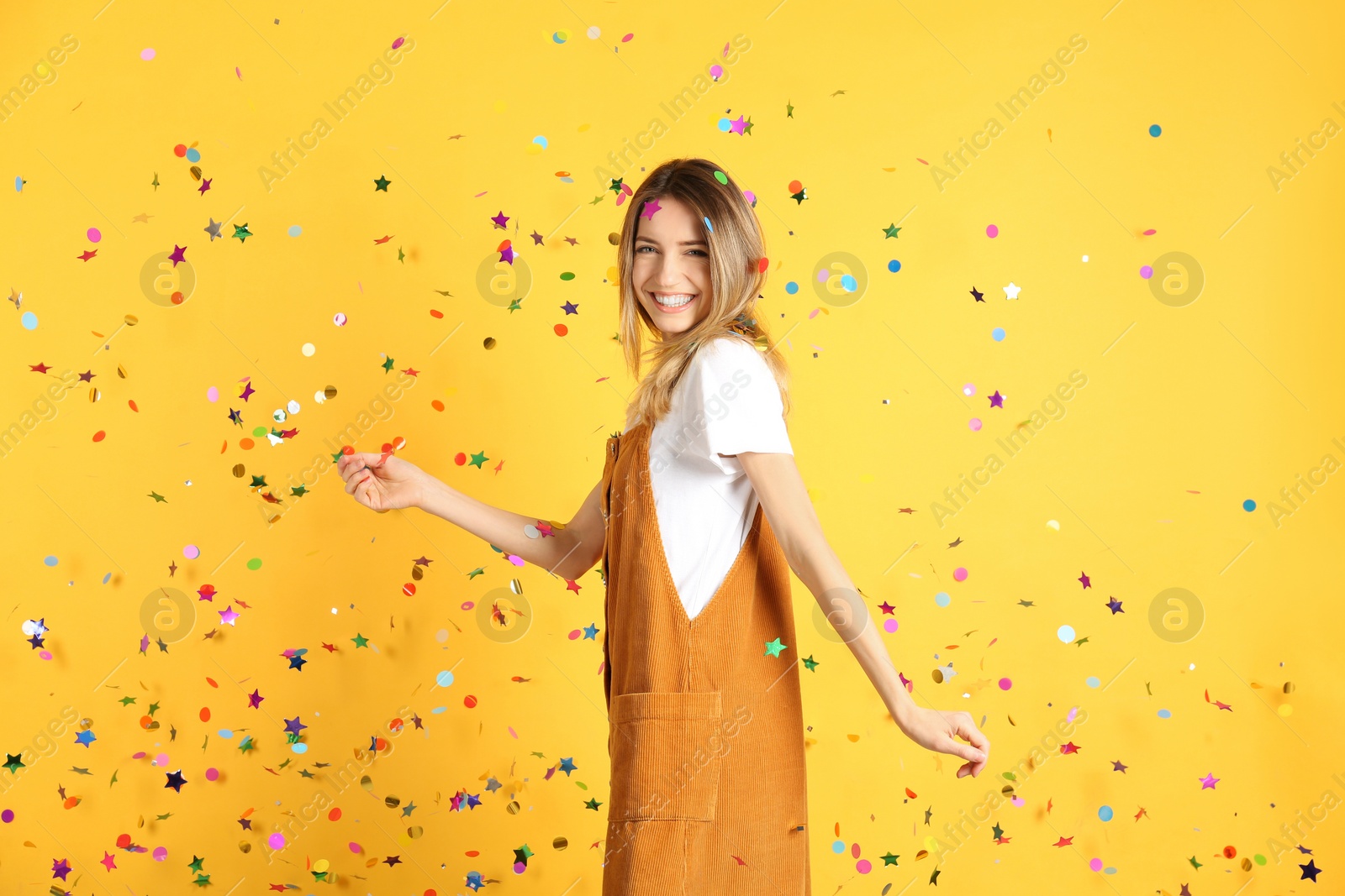 Photo of Happy woman and falling confetti on yellow background