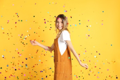 Happy woman and falling confetti on yellow background