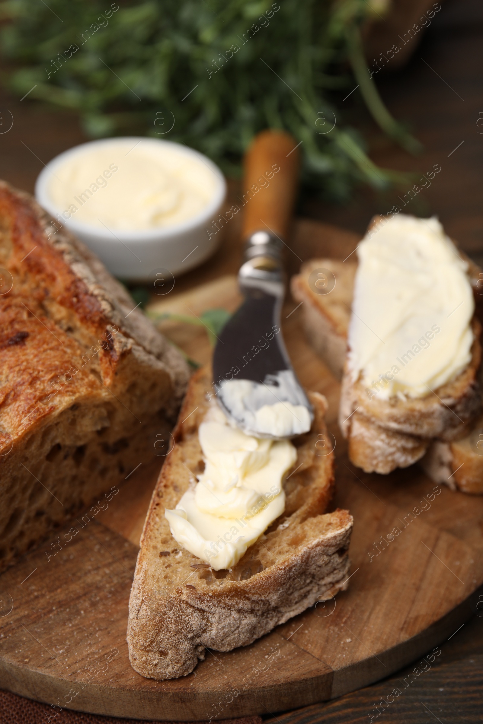 Photo of Tasty bread with butter and knife on wooden table, closeup. Space for text