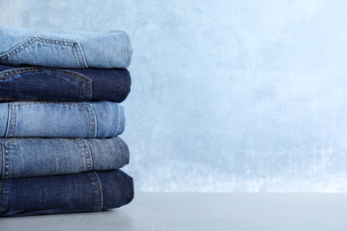 Stack of different jeans on light table against blue background. Space for text