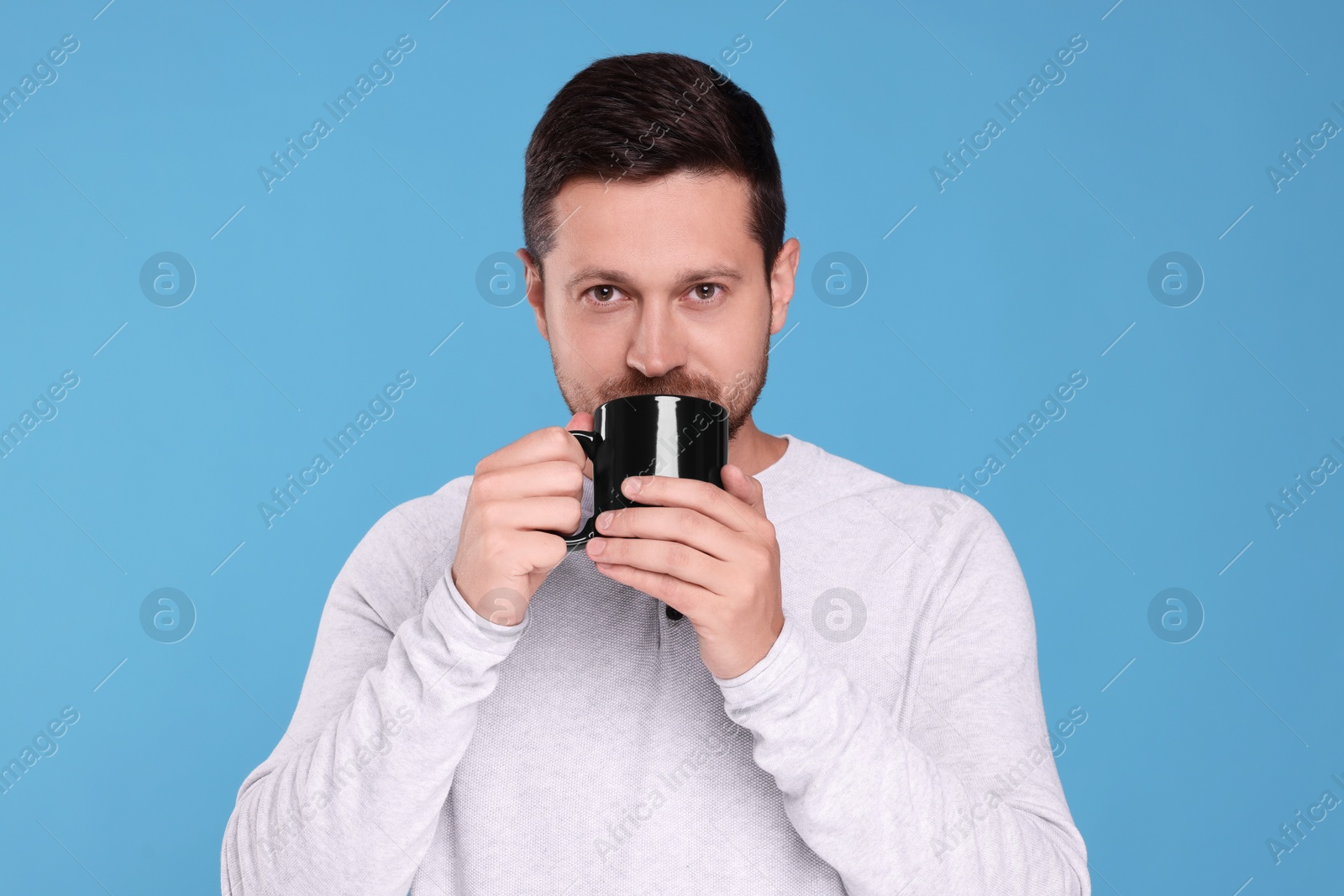 Photo of Portrait of man drinking from black mug on light blue background