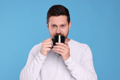 Portrait of man drinking from black mug on light blue background