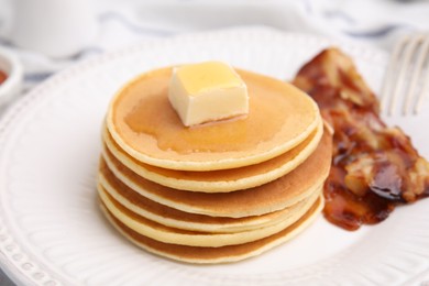 Photo of Delicious pancakes with butter, maple syrup and fried bacon on white marble table