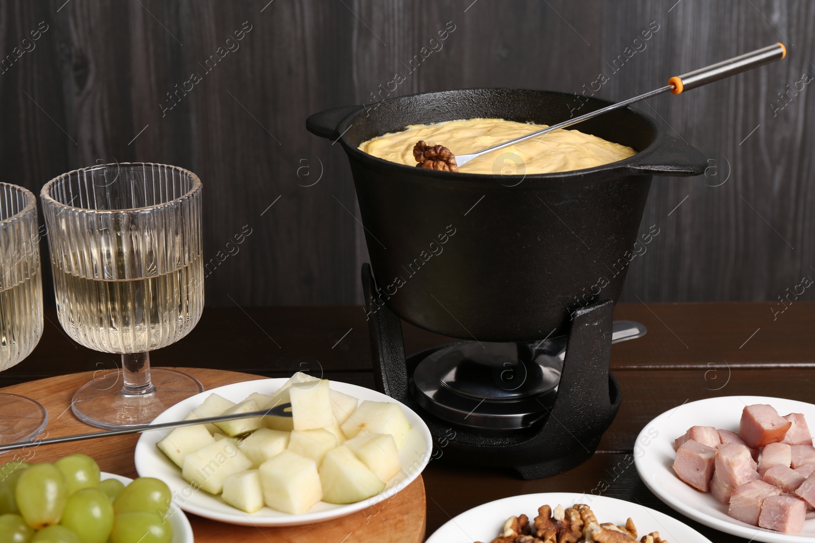 Photo of Fondue pot with tasty melted cheese, forks, wine and different snacks on wooden table