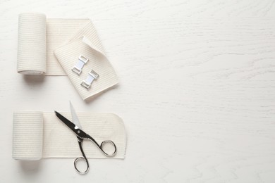 Photo of Medical bandage rolls and scissors on white wooden table, flat lay. Space for text