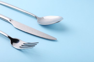 Photo of Stylish silver cutlery set on light blue background, closeup. Space for text