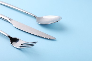 Stylish silver cutlery set on light blue background, closeup. Space for text