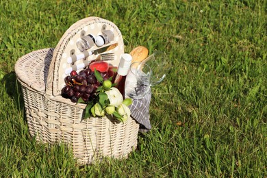 Photo of Picnic basket with tasty food, flowers and cider on grass. Space for text