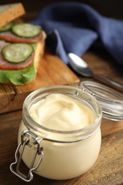 Photo of Jar of delicious mayonnaise near fresh sandwich on wooden table