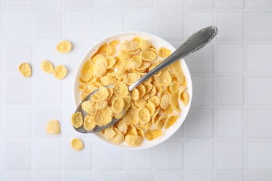 Photo of Breakfast cereal. Tasty corn flakes with milk in bowl and spoon on white tiled table, top view