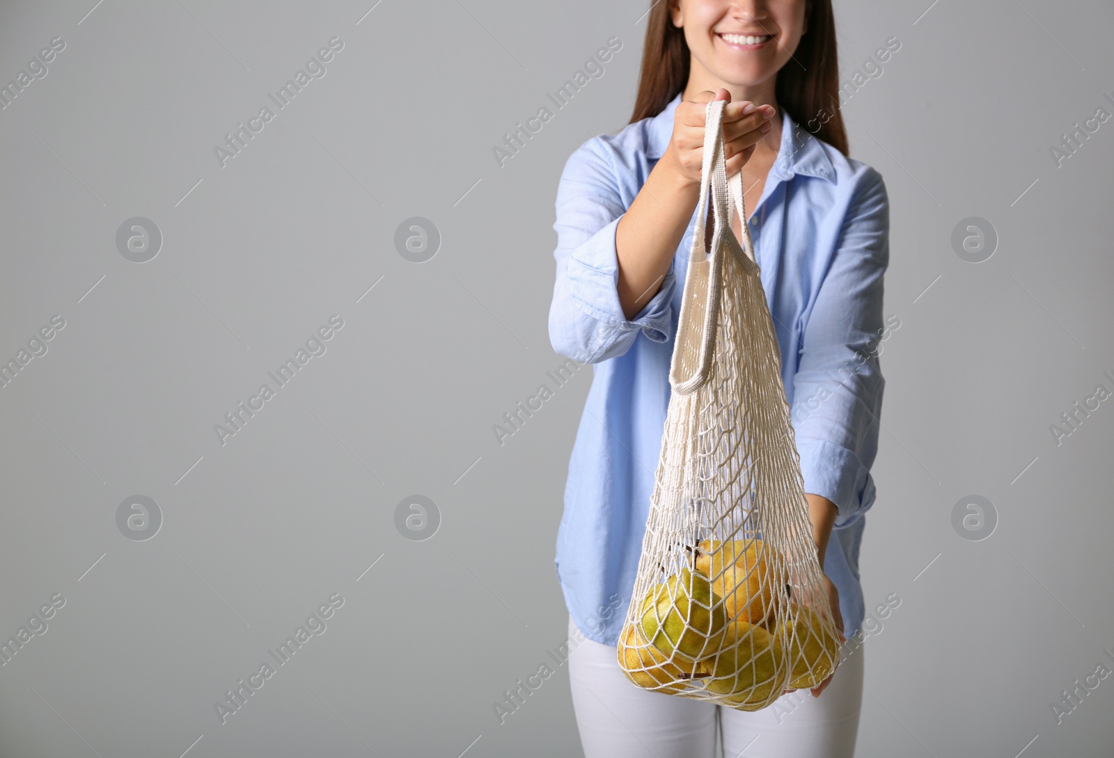 Photo of Woman holding net bag with fresh ripe pears on grey background, closeup. Space for text