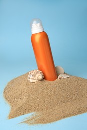 Photo of Sand with bottle of sunscreen, stone and seashell against light blue background. Sun protection