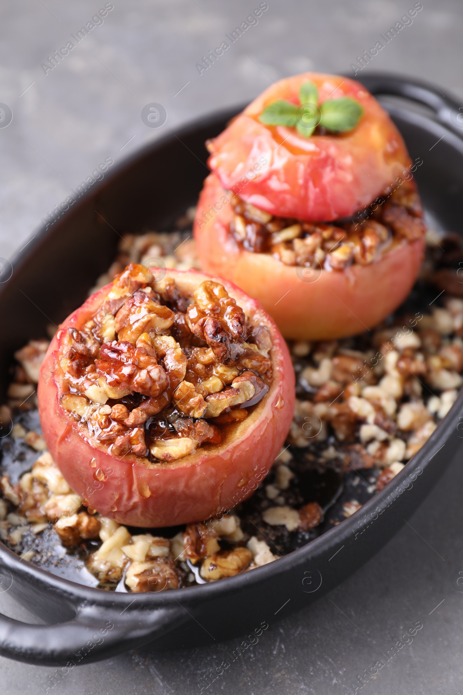 Photo of Tasty baked apples with nuts, honey and mint in baking dish on gray table, closeup