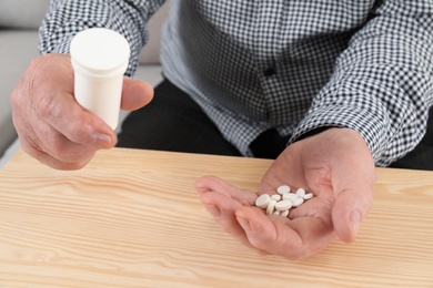 Photo of Senior man holding pills and bottle at table, closeup