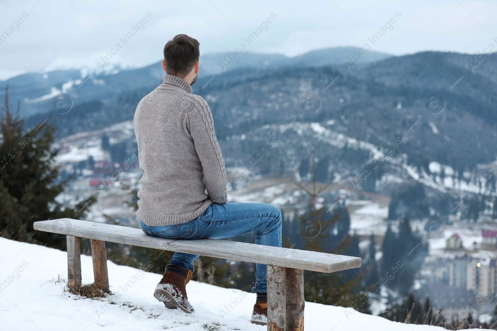 Photo of Man sitting on bench and enjoying mountain landscape, space for text. Winter vacation