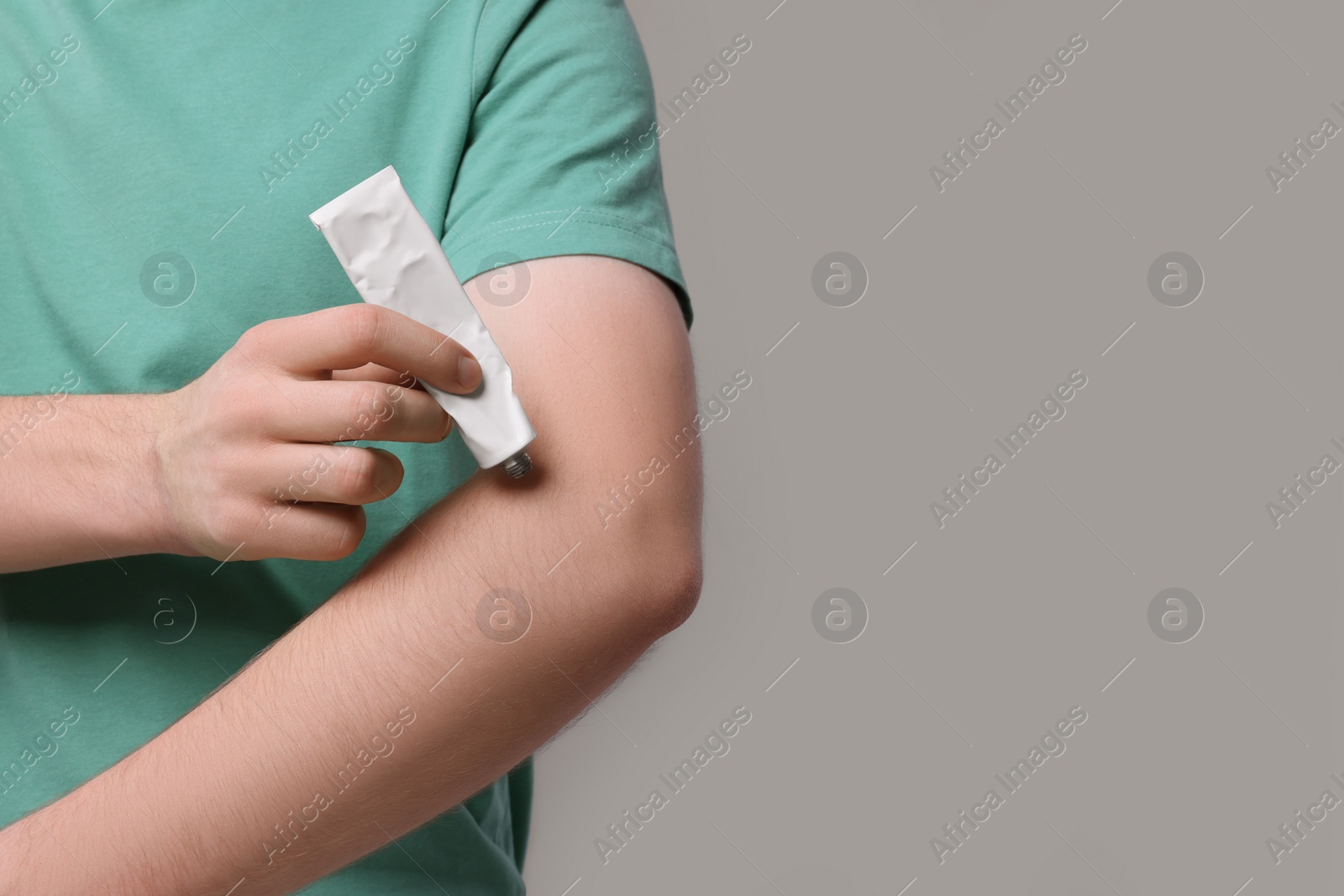 Photo of Man applying ointment from tube onto his arm on light grey background, closeup. Space for text