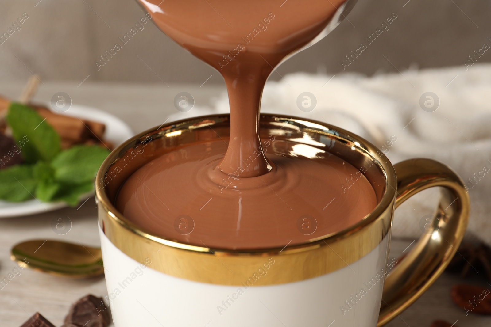 Photo of Pouring yummy hot chocolate into cup on table, closeup