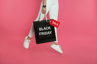 Woman jumping with shopping bag on pink background, closeup. Black Friday Sale