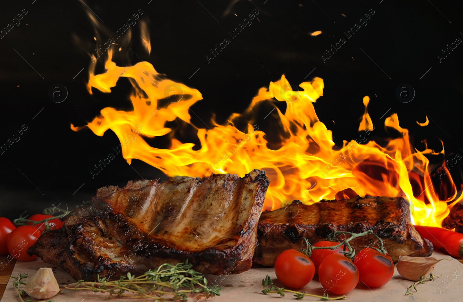 Image of Tasty grilled ribs with tomatoes on table and bright flame on background