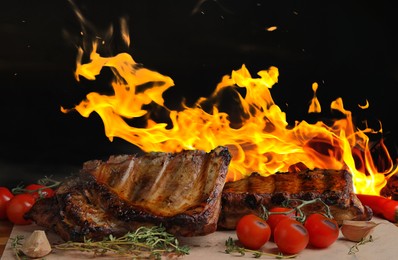 Image of Tasty grilled ribs with tomatoes on table and bright flame on background