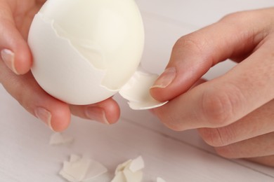 Woman peeling boiled egg at white table, closeup