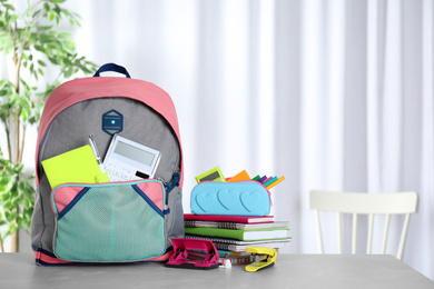 Photo of Stylish backpack with different school stationery on table indoors. Space for text