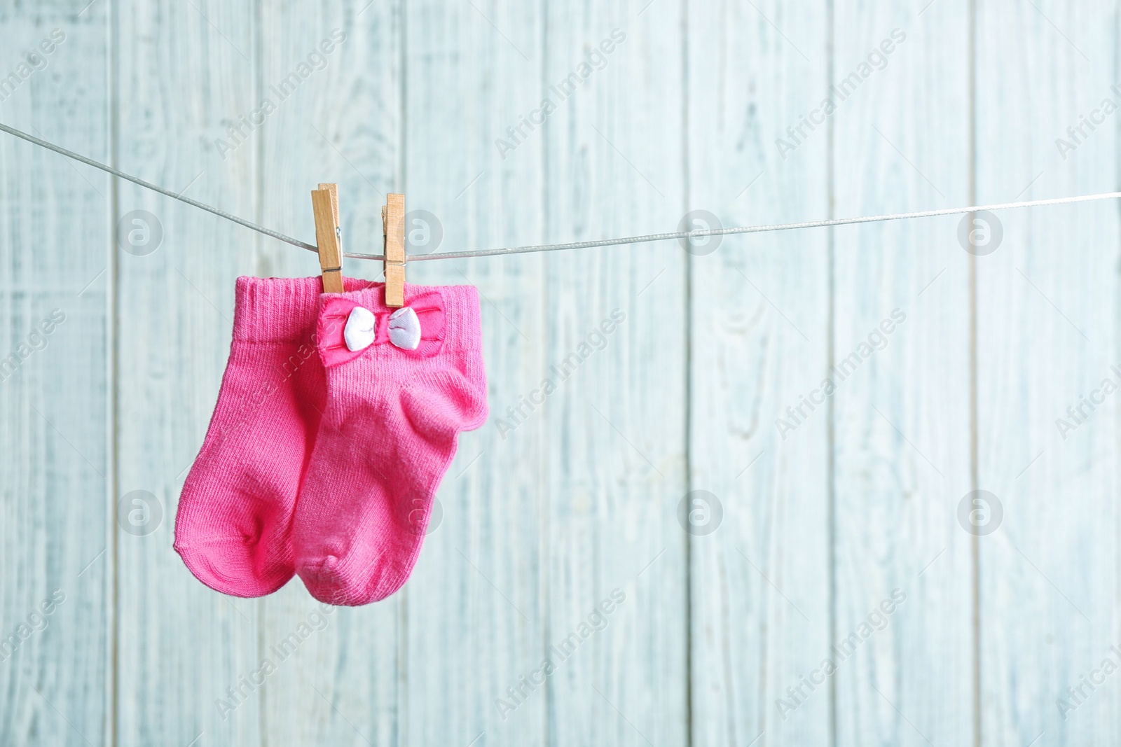 Photo of Pair of socks on laundry line against wooden background, space for text. Baby accessories