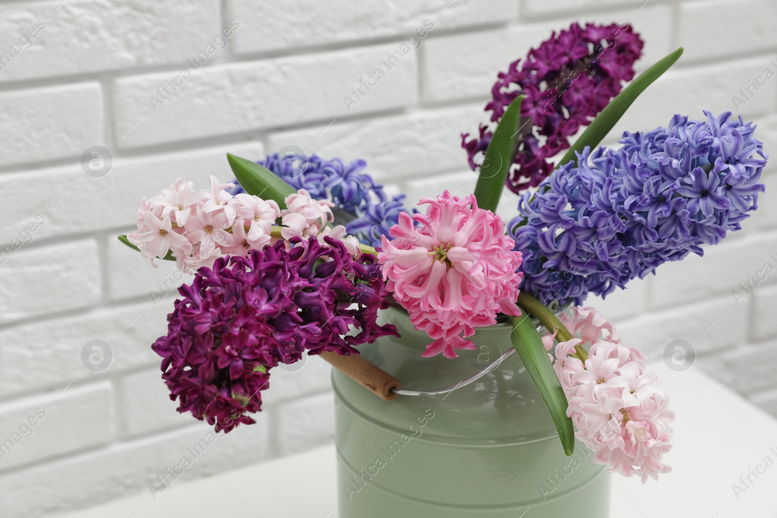 Photo of Beautiful hyacinths in metal can on table against brick wall. Spring flowers