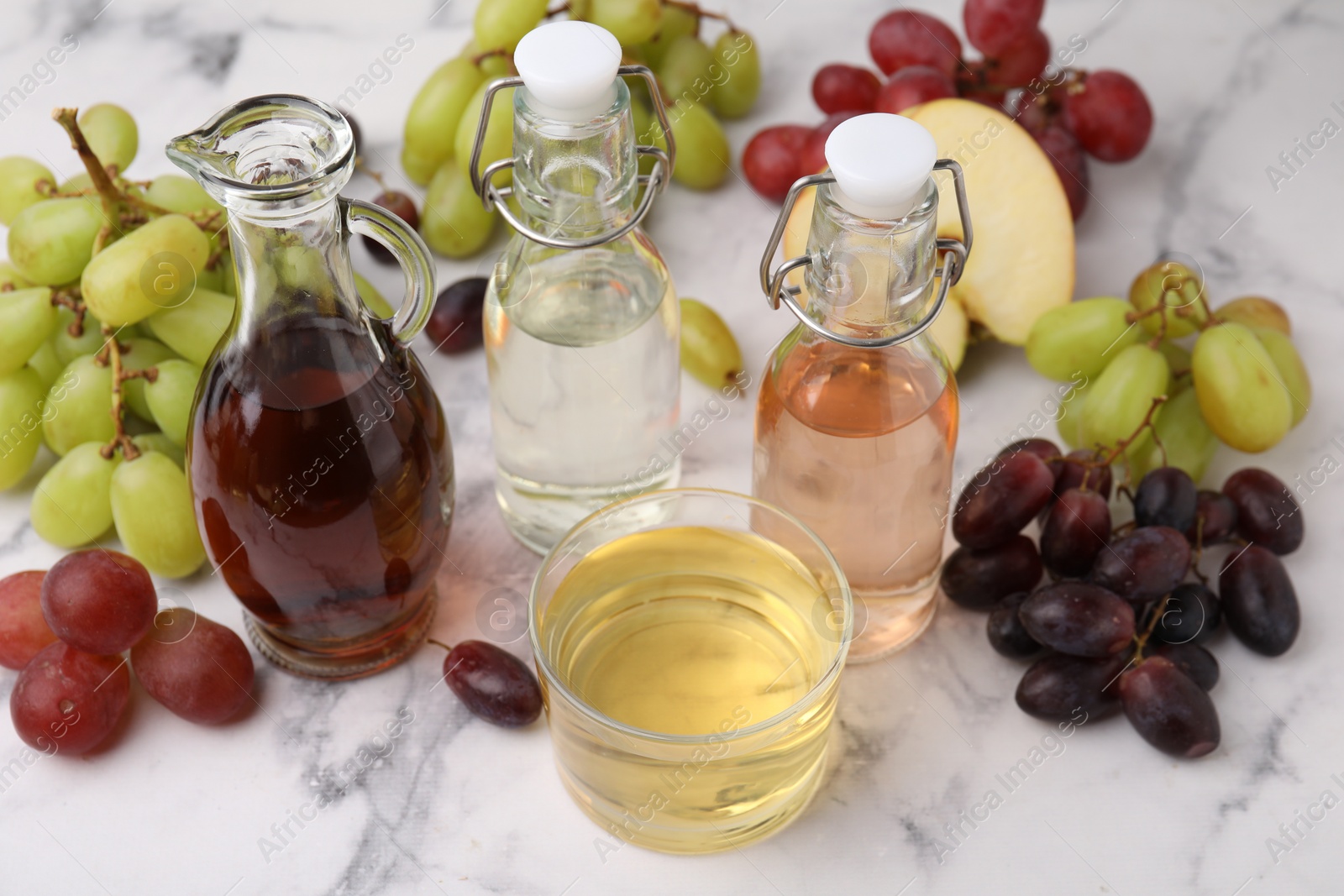 Photo of Different types of vinegar and grapes on light marble table, closeup