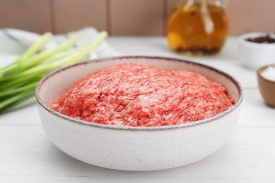 Bowl of raw fresh minced meat on white wooden table, closeup