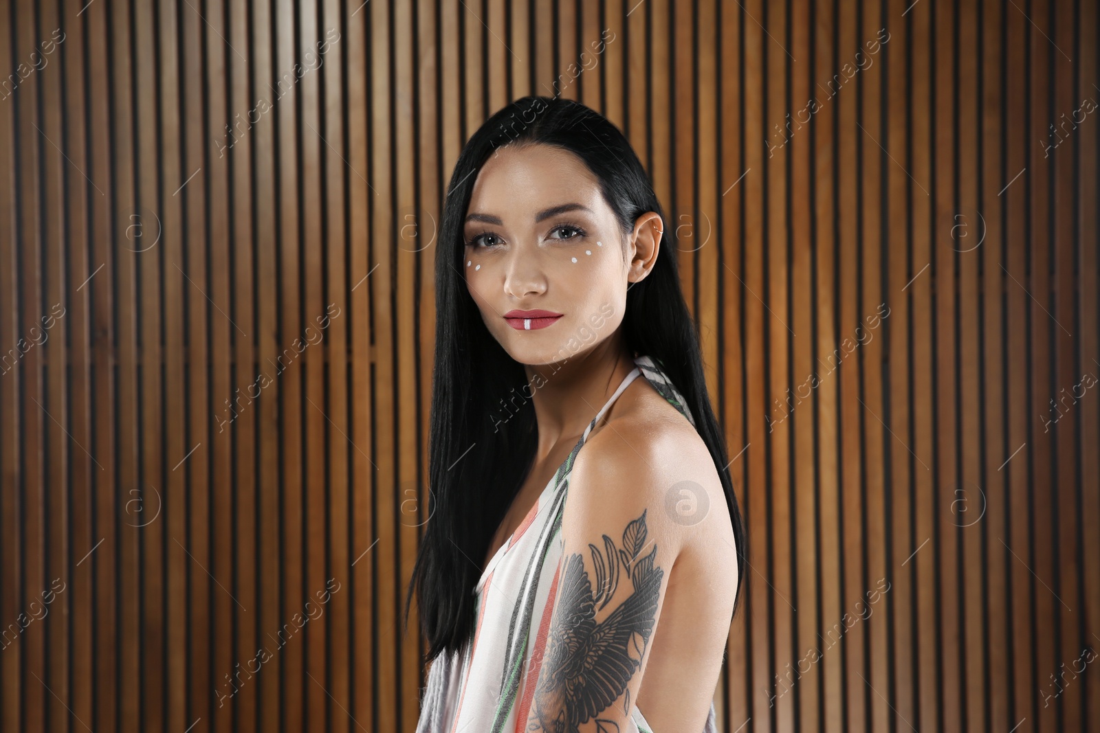 Photo of Portrait of young hippie woman with boho makeup in stylish outfit on wooden background